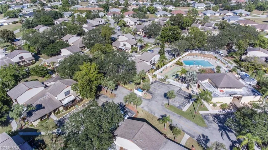 Aerial view of a residential community featuring a central swimming pool with surrounding patio, a tennis court, and mature landscaping