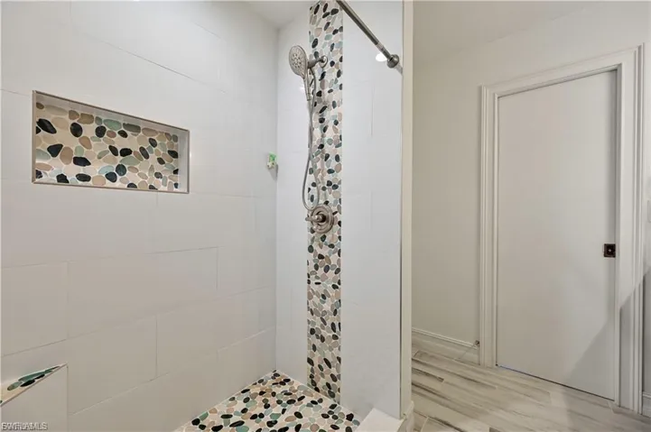 Walk-in shower featuring white subway tile, pebble tile accents, a recessed niche, a built-in bench, and a brushed nickel shower head
