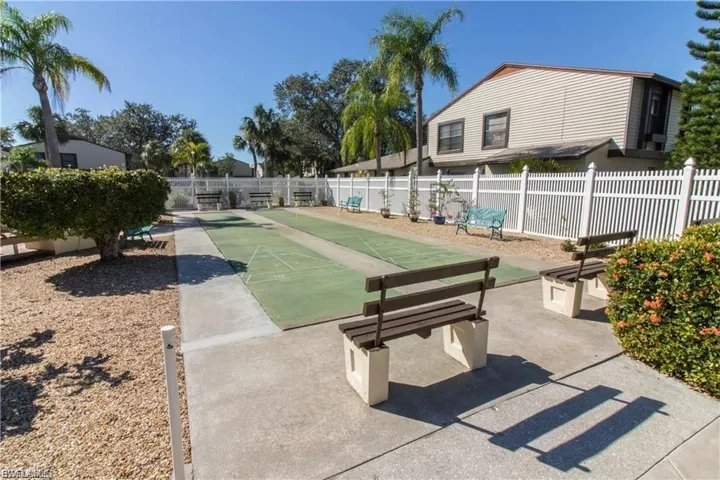 Dual shuffleboard courts, concrete pathways, and a white picket fence create a structured outdoor space