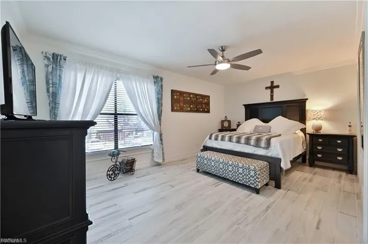 Spacious room featuring light wood-finish flooring, a large window with horizontal blinds, crown molding, and a ceiling fan with integrated lighting