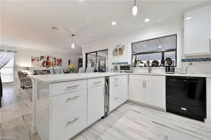 Contemporary kitchen featuring a large island with integrated wine refrigerator, white cabinetry, undermount sink, and black dishwasher