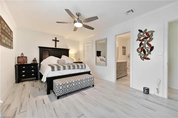 Spacious sleeping area featuring light wood-finish flooring, crown molding, and a ceiling fan with integrated lighting
