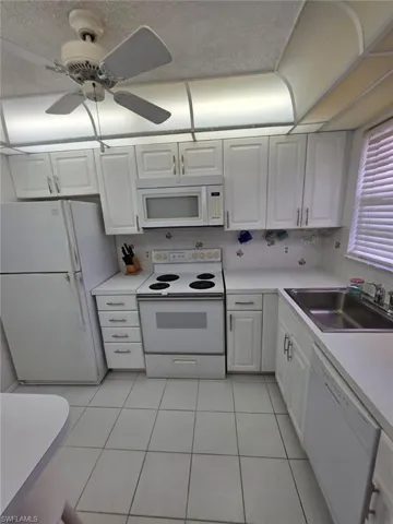 Kitchen featuring white appliances, white cabinetry, light countertops, light tile patterned floors, and backsplash