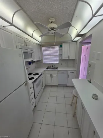 Kitchen with white appliances, white cabinets, light countertops, and a textured ceiling
