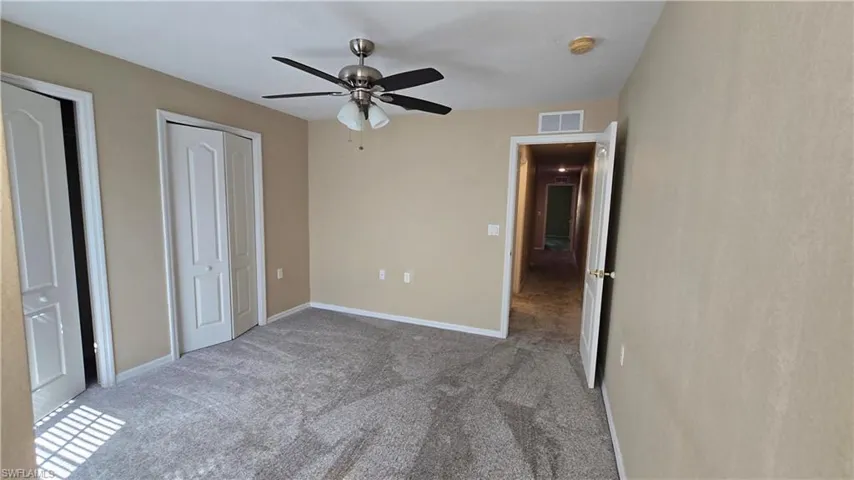 Unfurnished bedroom with carpet floors, a ceiling fan, and multiple closets