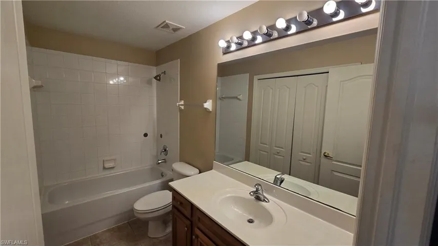 Bathroom featuring bathtub / shower combination, vanity, a closet, and dark tile patterned floors