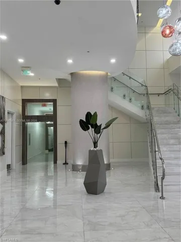 Lobby area featuring polished tile flooring, a prominent staircase with glass railings, and a large central column with integrated lighting
