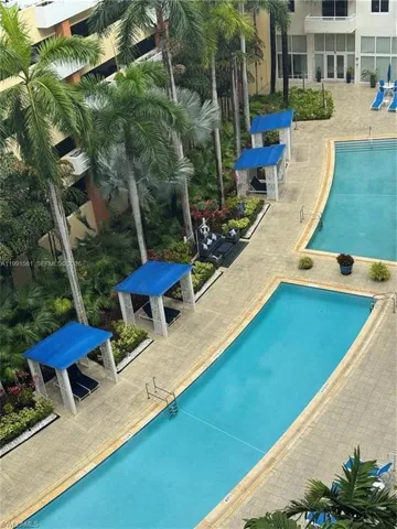 Outdoor aquatic area featuring two rectangular pools, a surrounding paver deck, and multiple cabanas with blue canopies