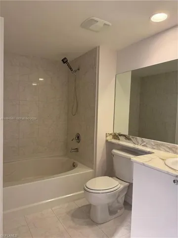 Bathroom featuring a bathtub with shower, tiled surround, white vanity with stone-finish countertop, and recessed lighting
