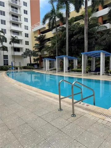 Resort-style outdoor pool featuring a tiled deck, three shaded cabanas, and prominent palm trees