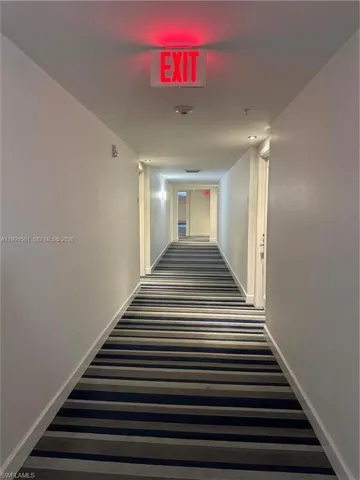 Hallway featuring striped carpet flooring in shades of blue and gray, white walls, and white baseboards