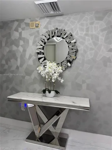 Textured wall finish, mirrored wall decor, polished chrome console table, marble-look countertop, and white tile flooring