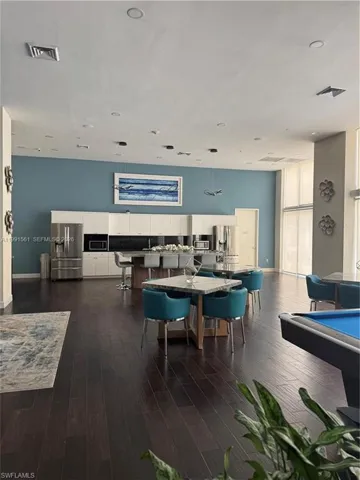 Spacious common area featuring dark wood-finish flooring, a full kitchen with stainless steel appliances and white cabinetry, a large center island with bar seating, and recessed lighting throughout