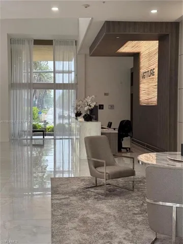 Lobby area featuring large format polished tile flooring, full-height windows with sheer drapery, and a reception desk with back-lit wall paneling