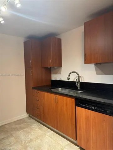 Kitchen featuring wood-finish cabinetry, dark stone countertops, and a stainless steel sink with a gooseneck faucet