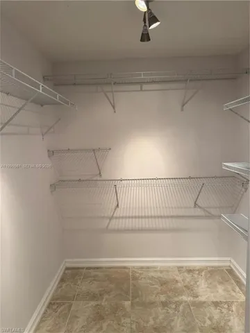 Walk-in closet featuring track lighting, multiple wire shelving units, and large format tiled flooring