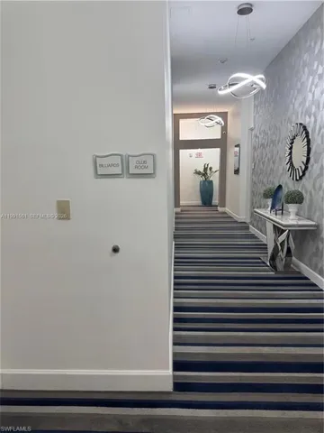 Hallway featuring striped carpet, contemporary pendant lighting, and textured wall covering