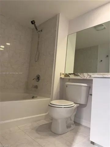 Bathroom featuring a white bathtub with a showerhead, a toilet, a vanity with a mirror, and tiled flooring