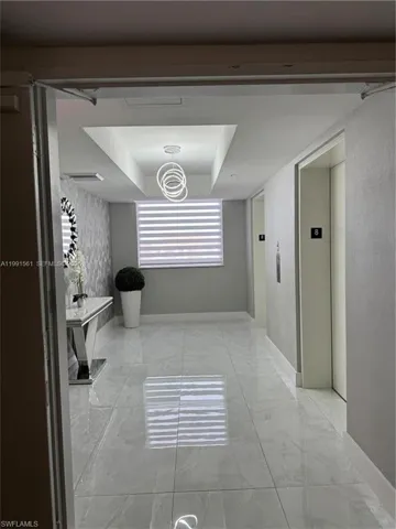 Polished light-toned tile flooring extends through this interior hall, featuring a modern ring chandelier set within a recessed ceiling detail