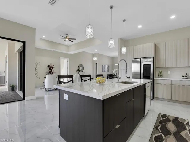 Kitchen featuring a kitchen island with sink, pendant lighting, light brown cabinets, sink, and light stone countertops