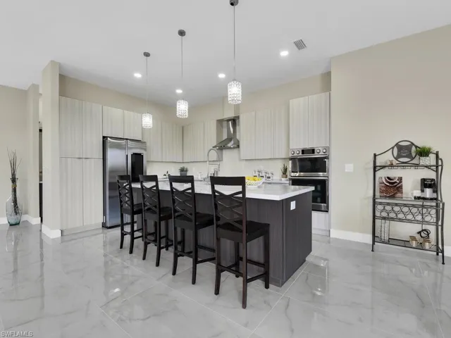 Kitchen with an island with sink, hanging light fixtures, wall chimney exhaust hood, appliances with stainless steel finishes, and a breakfast bar