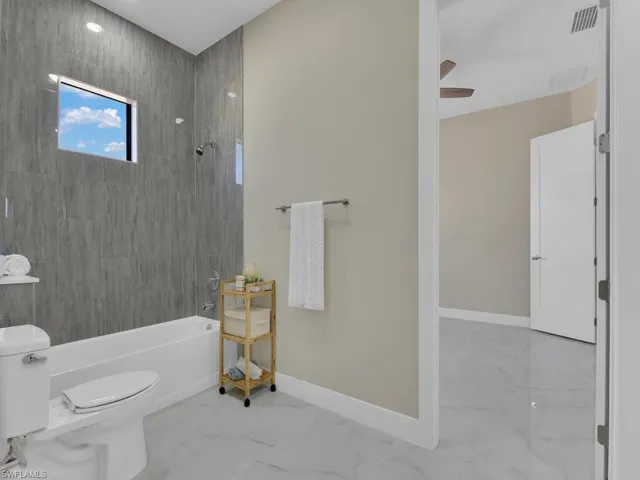 Bathroom featuring ceiling fan, tiled shower / bath, and toilet