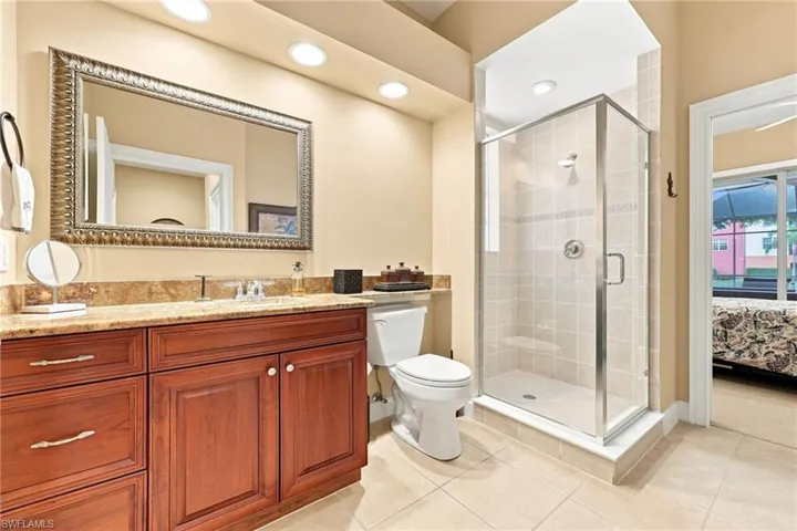 Spa-inspired primary bathroom featuring a wood-finish vanity with dual sinks, granite countertop, and polished chrome hardware