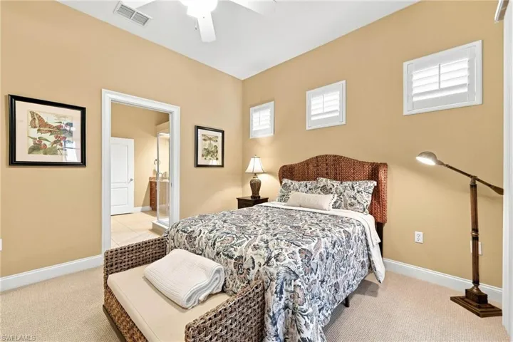 Spacious primary bedroom showcasing warm neutral walls, abundant natural light from multiple transom windows, a decorative upholstered bed frame, ceiling fan, hardwood flooring, and woven storage benches