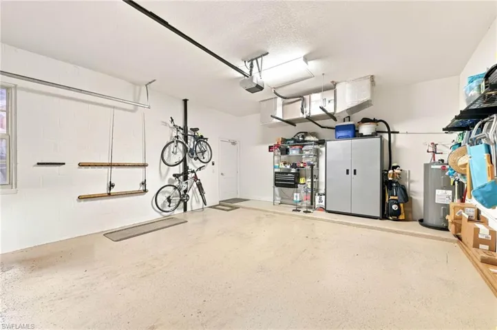 Spacious garage featuring epoxy-coated concrete flooring, abundant natural lighting from overhead fixtures, wall-mounted bike storage system, built-in cabinetry and shelving units, and ample room for vehicles and equipment storage