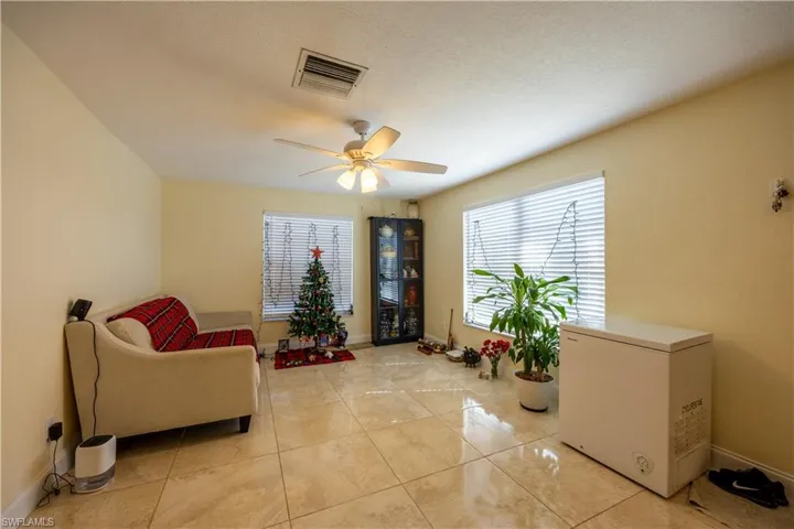 Spacious interior featuring neutral wall paint, tiled flooring, a ceiling fan with integrated lighting, and multiple windows with blinds