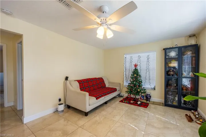 Living area featuring neutral-toned walls, tile flooring, a window with blinds, and a ceiling fan with integrated lighting