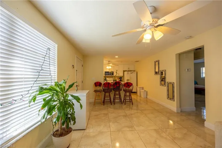 Spacious interior room featuring large format tile flooring, a ceiling fan with integrated lighting, and a wide window with blinds