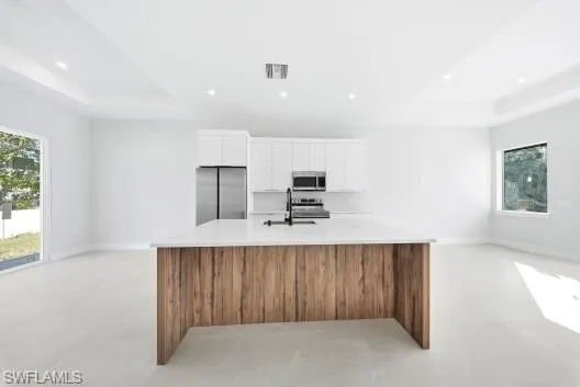 Kitchen featuring open floor plan, white cabinets, a raised ceiling, brown cabinetry, and recessed lighting