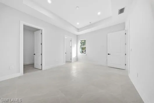 Unfurnished bedroom featuring concrete flooring, a raised ceiling, and recessed lighting