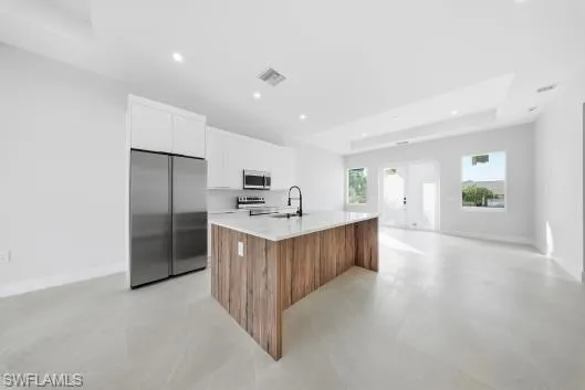 Kitchen with brown cabinets, stainless steel appliances, white cabinets, finished concrete floors, and recessed lighting