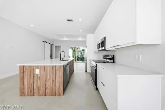 Kitchen with a barn door, white cabinets, stainless steel appliances, modern cabinets, and recessed lighting
