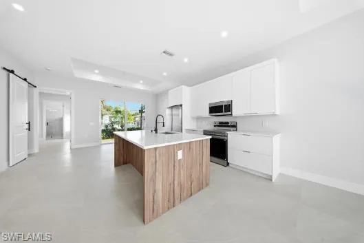 Kitchen with a barn door, white cabinetry, concrete floors, stainless steel appliances, and recessed lighting