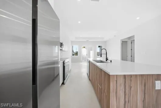 Kitchen with appliances with stainless steel finishes, brown cabinets, white cabinets, modern cabinets, and finished concrete flooring