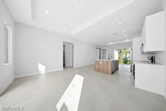 Kitchen with white cabinetry, open floor plan, finished concrete floors, a kitchen island with sink, and recessed lighting