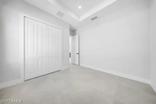 Unfurnished bedroom with finished concrete floors, a closet, a tray ceiling, and recessed lighting