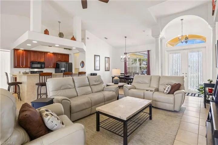 Living room with high vaulted ceiling, a chandelier, light tile patterned flooring, and a ceiling fan