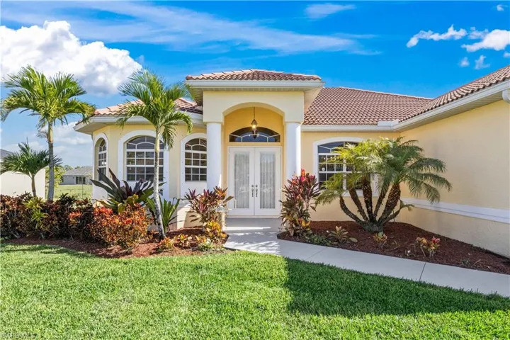 View of exterior entry with french doors, a tiled roof, a yard, and stucco siding
