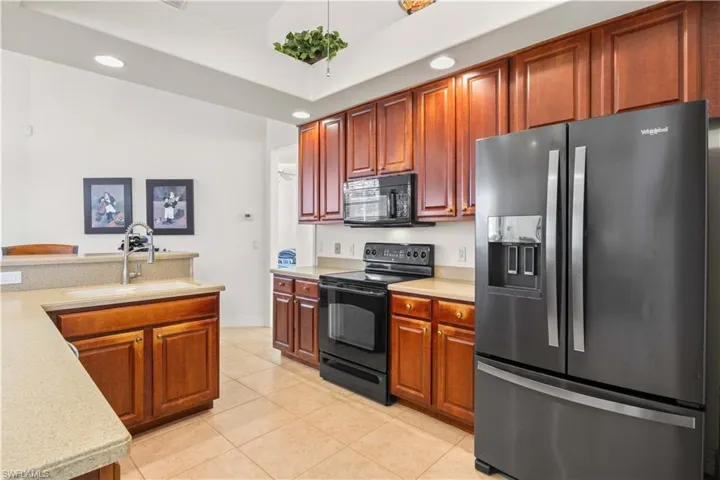 Kitchen with black appliances, recessed lighting, light tile patterned flooring, and light stone countertops