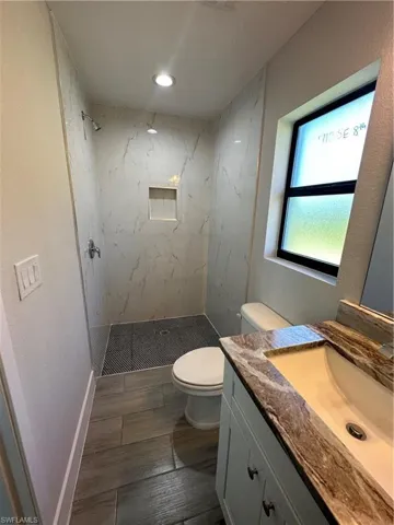 Bathroom featuring vanity, tiled shower, toilet, and tile patterned flooring