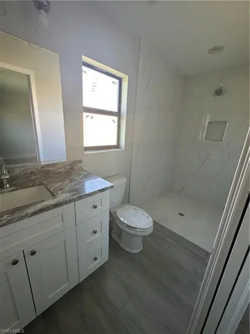 Bathroom featuring tiled shower, tile patterned flooring, toilet, and vanity