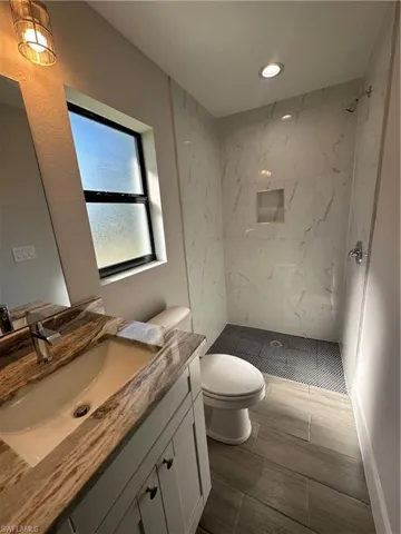 Bathroom featuring toilet, vanity, and a tile shower