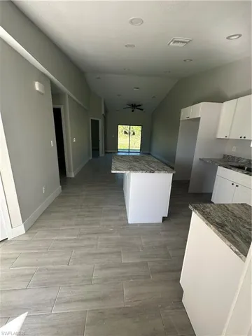 Kitchen with white cabinets, vaulted ceiling, light tile patterned floors, a center island, and ceiling fan
