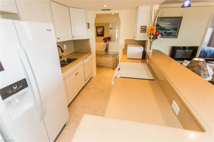 Kitchen featuring white appliances, white cabinets, sink, light tile patterned floors, and tasteful backsplash