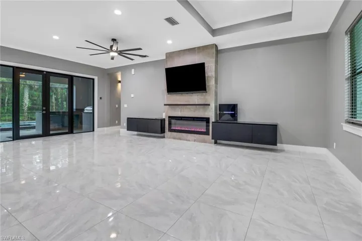 Unfurnished living room with ceiling fan, a raised ceiling, french doors, a tiled fireplace, and light tile patterned floors