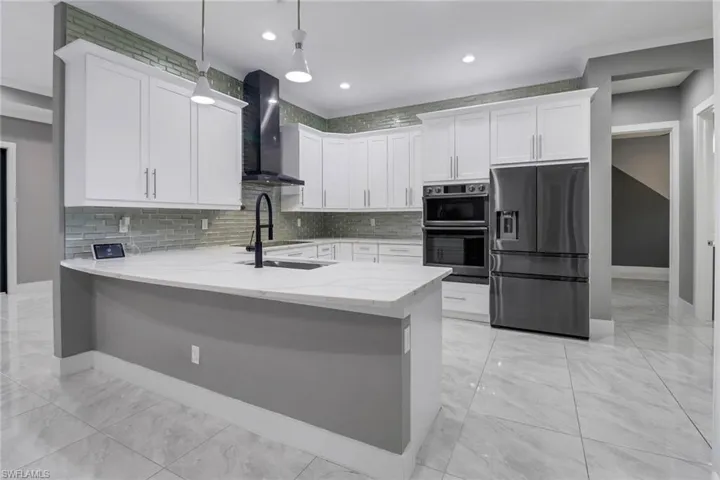 Kitchen featuring wall chimney exhaust hood, white cabinets, light tile patterned floors, decorative light fixtures, and stainless steel appliances
